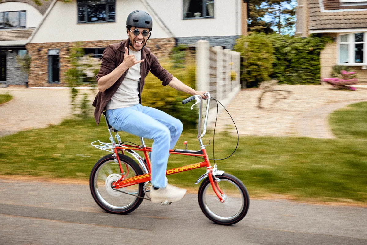 Man riding red Raleigh Chopper smiling.