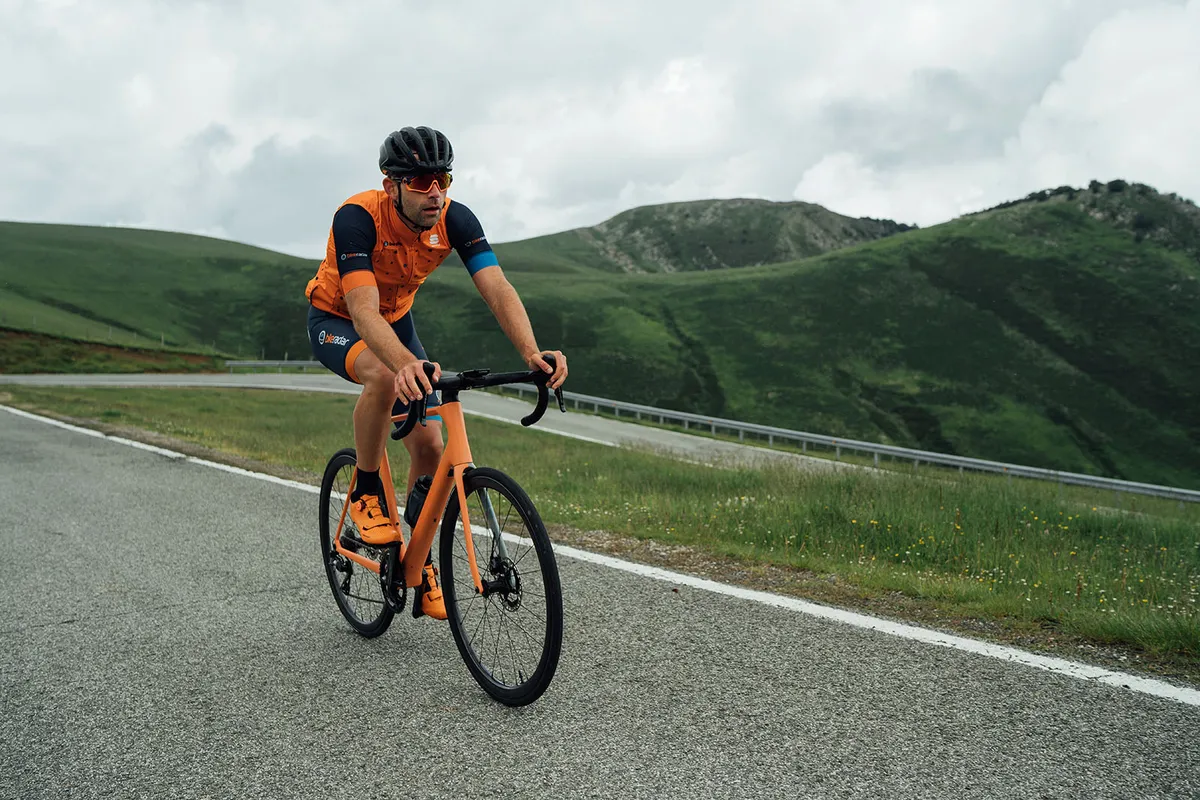 Male cyclist in orange top riding the Orbea Orca M10i LTD OMX road bike