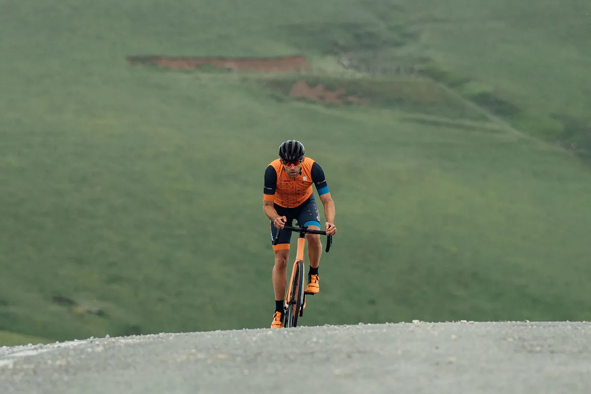 Male cyclist in orange top riding the Orbea Orca M10i LTD OMX road bike