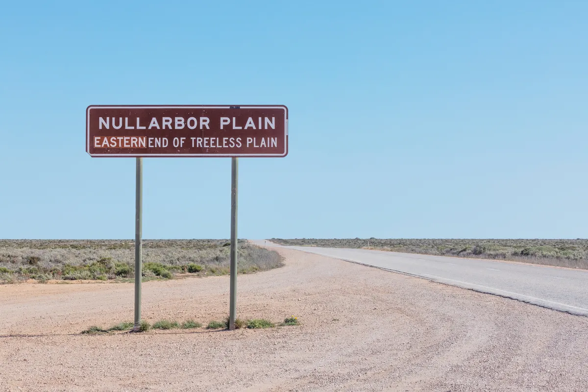 Nullarbor Plain sign. Eastern end of treeless plain sign. Eyre Highway. South Australia. Remote flat landscape. Blue sky with copy space.