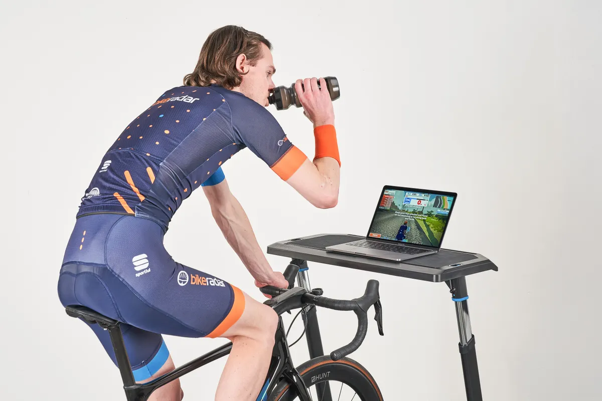 Simon von Bromley of BikeRadar drinking from a water bottle while riding a Wahoo smart trainer and using Zwift
