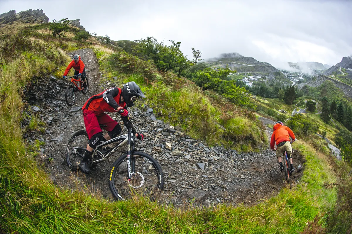 Three riders descending rocky trail at Antur Stiniog bike park