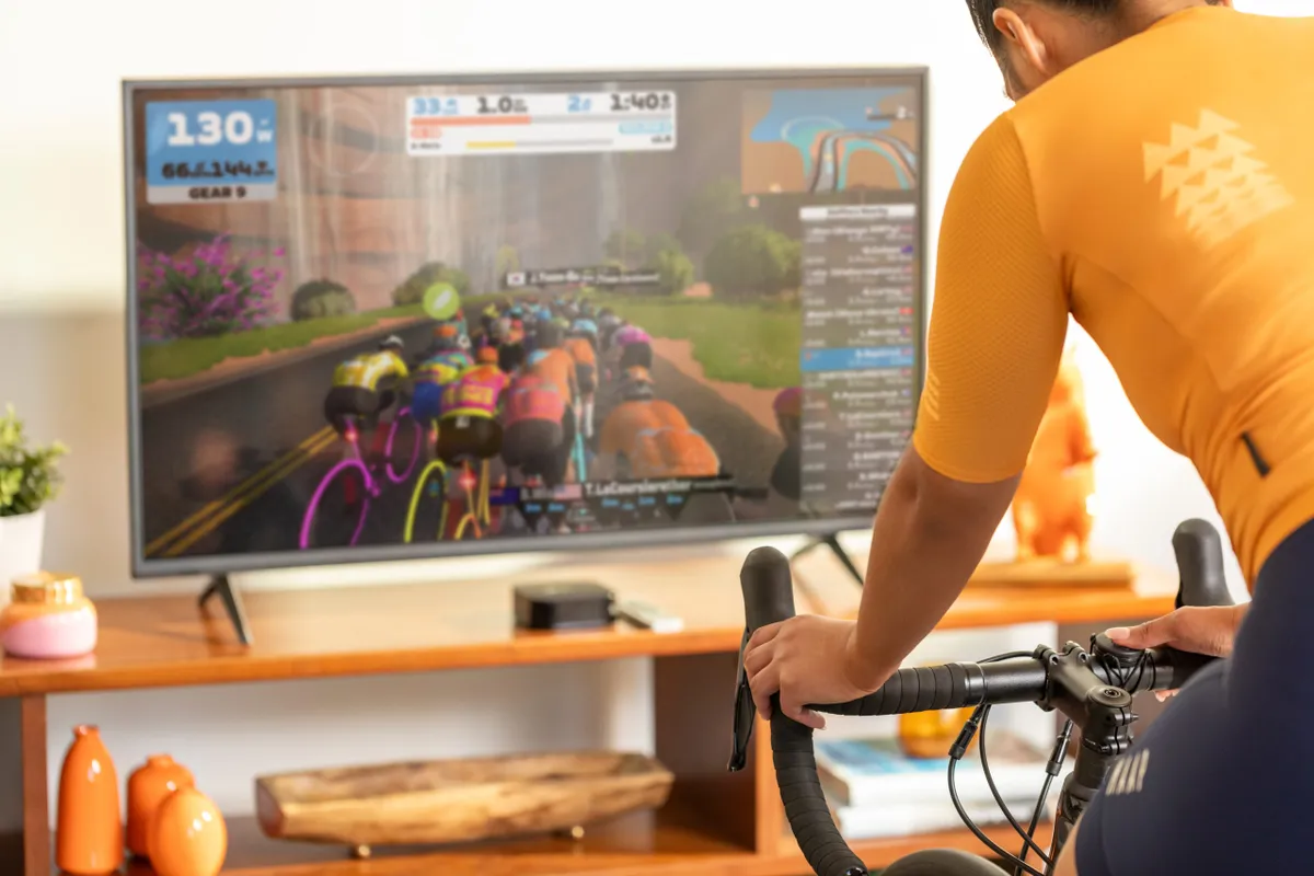 Screen showing Zwift race in background and cyclist on turbo trainer in foreground