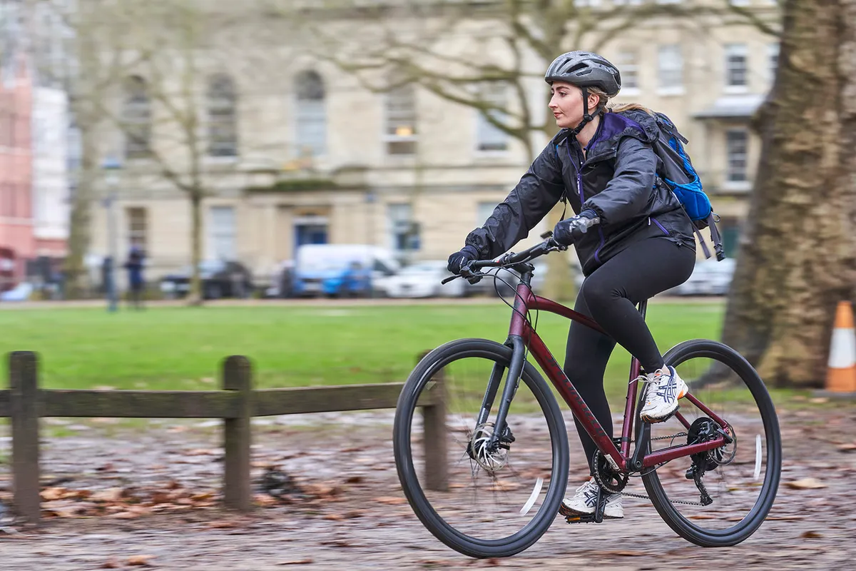 Female cyclist in dark purple jacket riding the Specialized Sirrus X 3.0 commuter bike