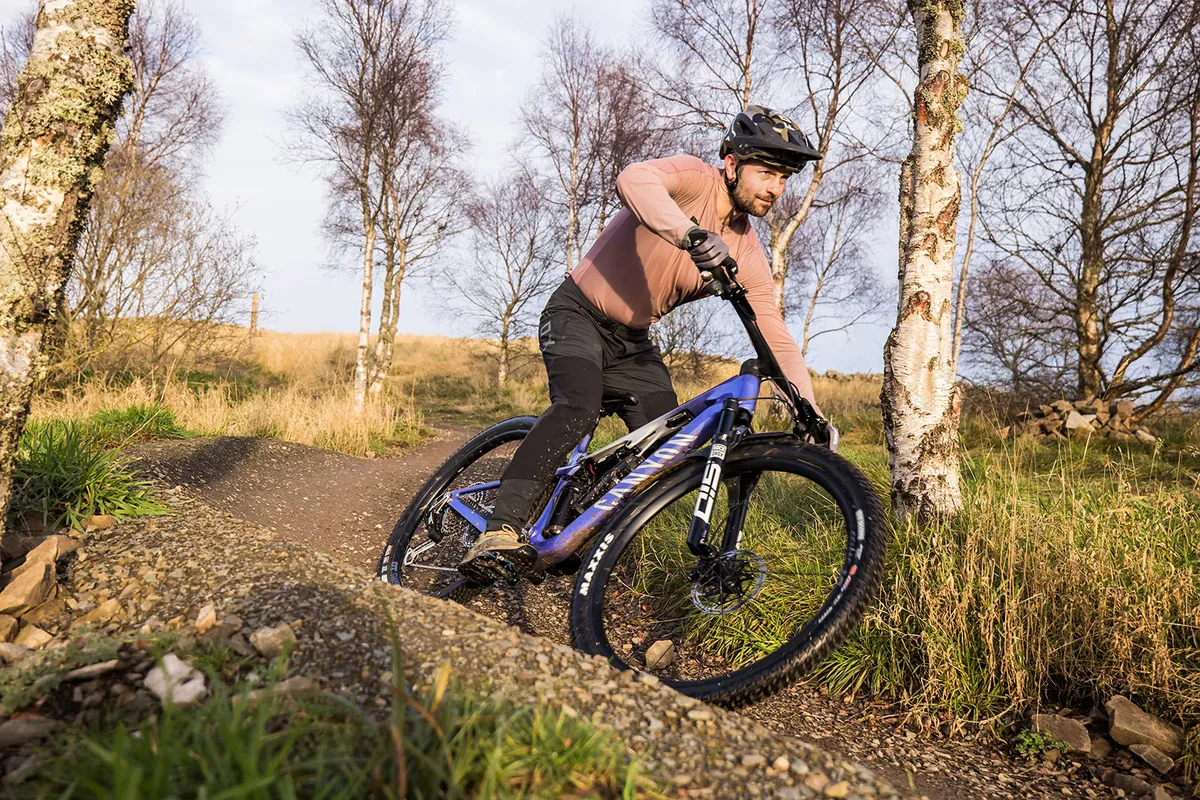 Male rider in light purple top riding the Canyon Lux Trail CFR LTD downcountry full suspension mountain bike