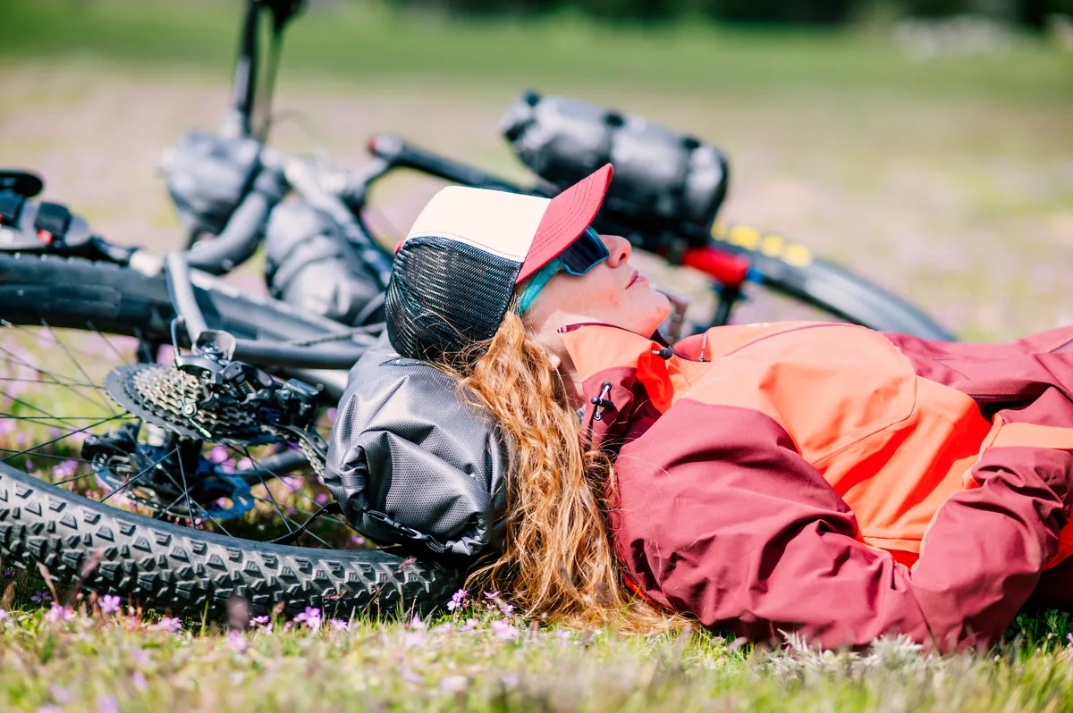 A woman lying on her mountain bike in a green meadow in spring
