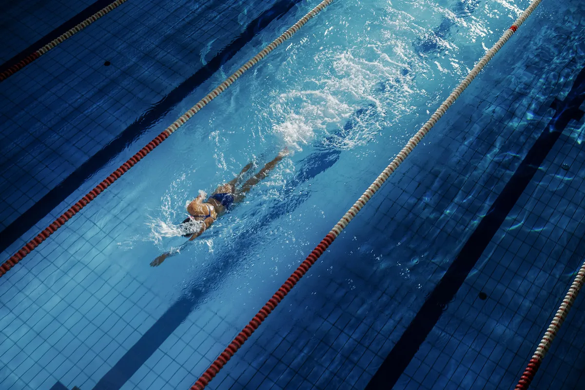 Female Swimmer Racing in Swimming Pool. Professional Athlete Overcoming Stress and Hardships in Dark Dramatic Pool
