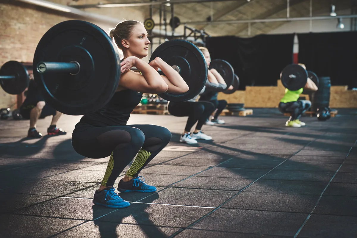 Young woman lifting barbells looking focused, working out in a gym with other people