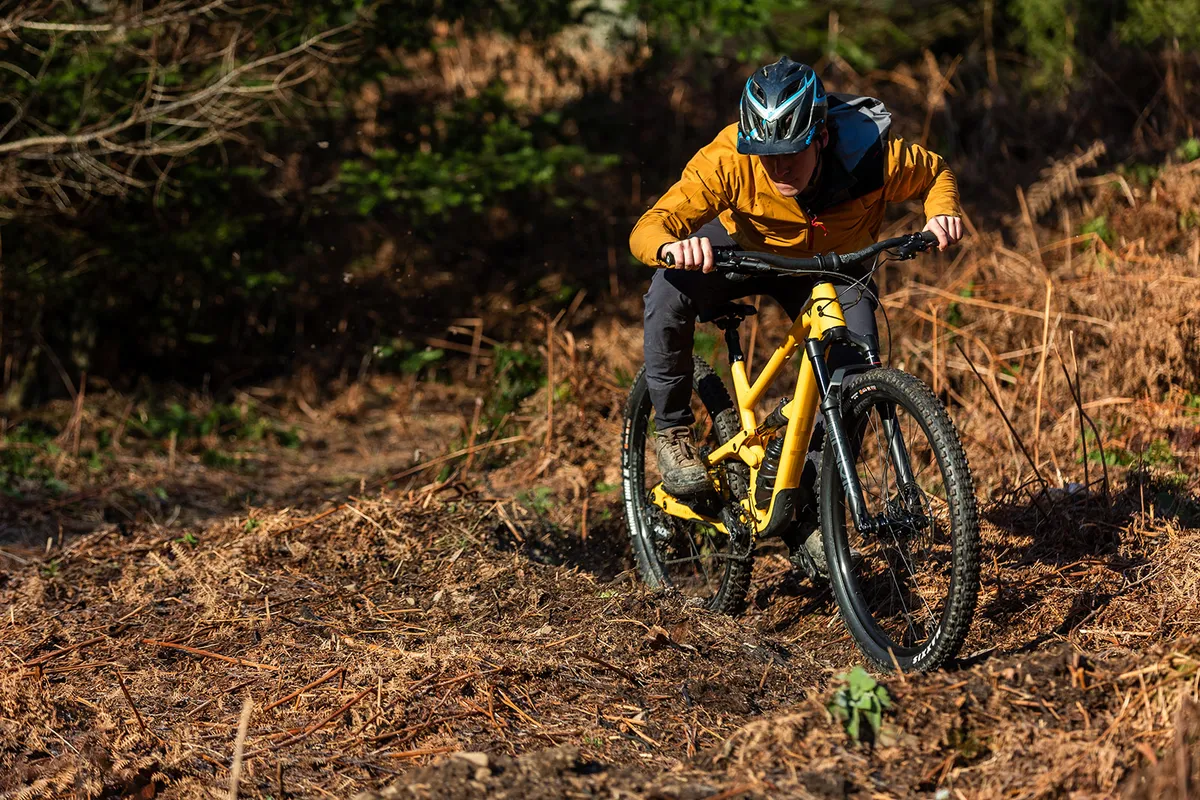 Male rider in mustard coloured top riding the YT Jeffsy Core 1 full suspension trail mountain bike through woodland