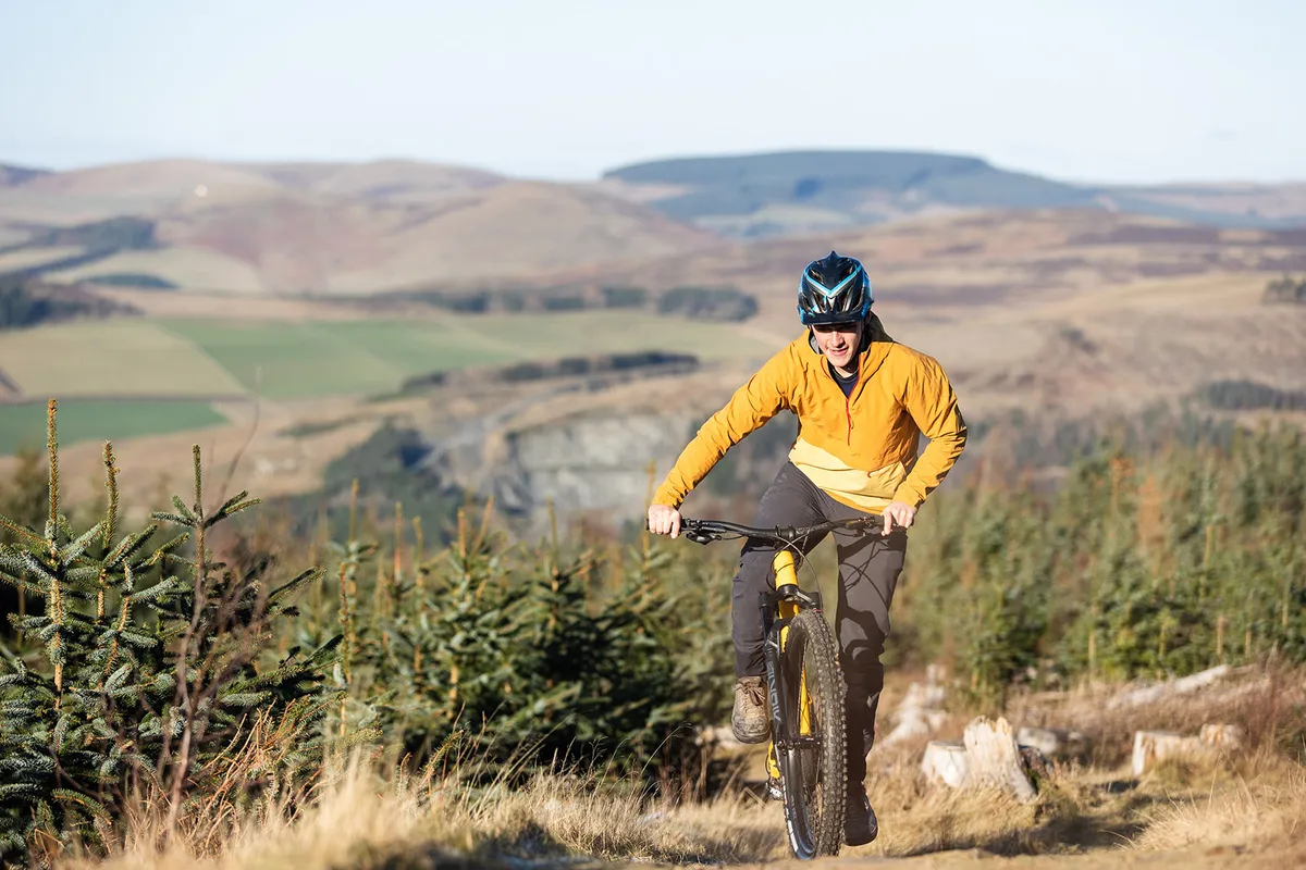 Male rider in mustard coloured top riding the YT Jeffsy Core 1 full suspension trail mountain bike through woodland