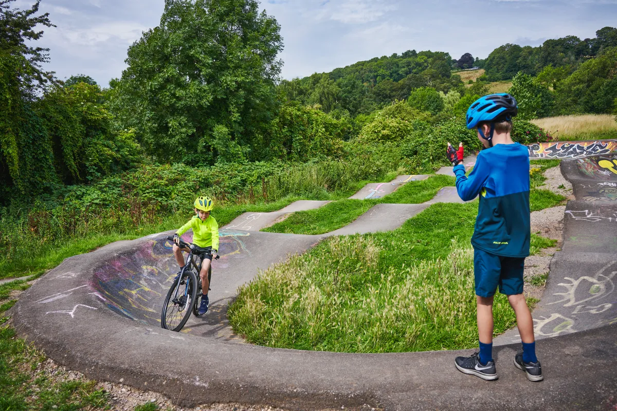 Young boy riding on pump track encouraged by another boy