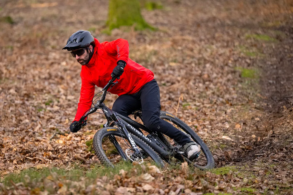 Male rider in red top riding the Atherton AM.130.1 full suspension mountain bike through woodland