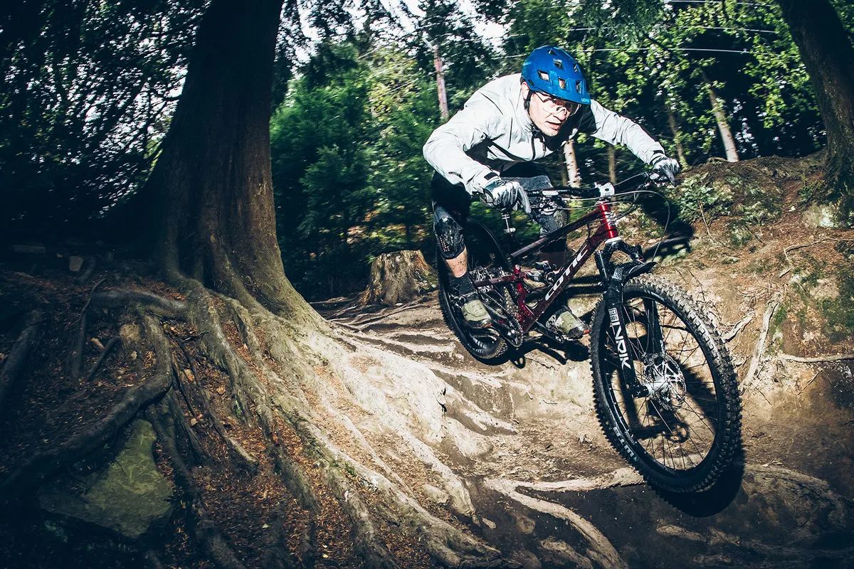 Male rider in grey top riding the Cotic Jeht Gen 2 XT Gold custom full suspension mountain bike through woodland