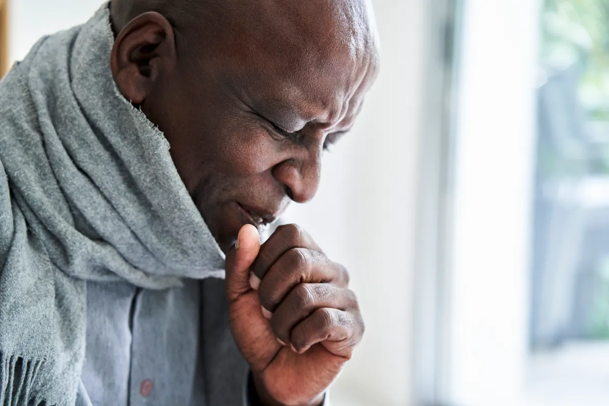 Portrait of visibly ill African-American man wearing scarf and coughing in his hand