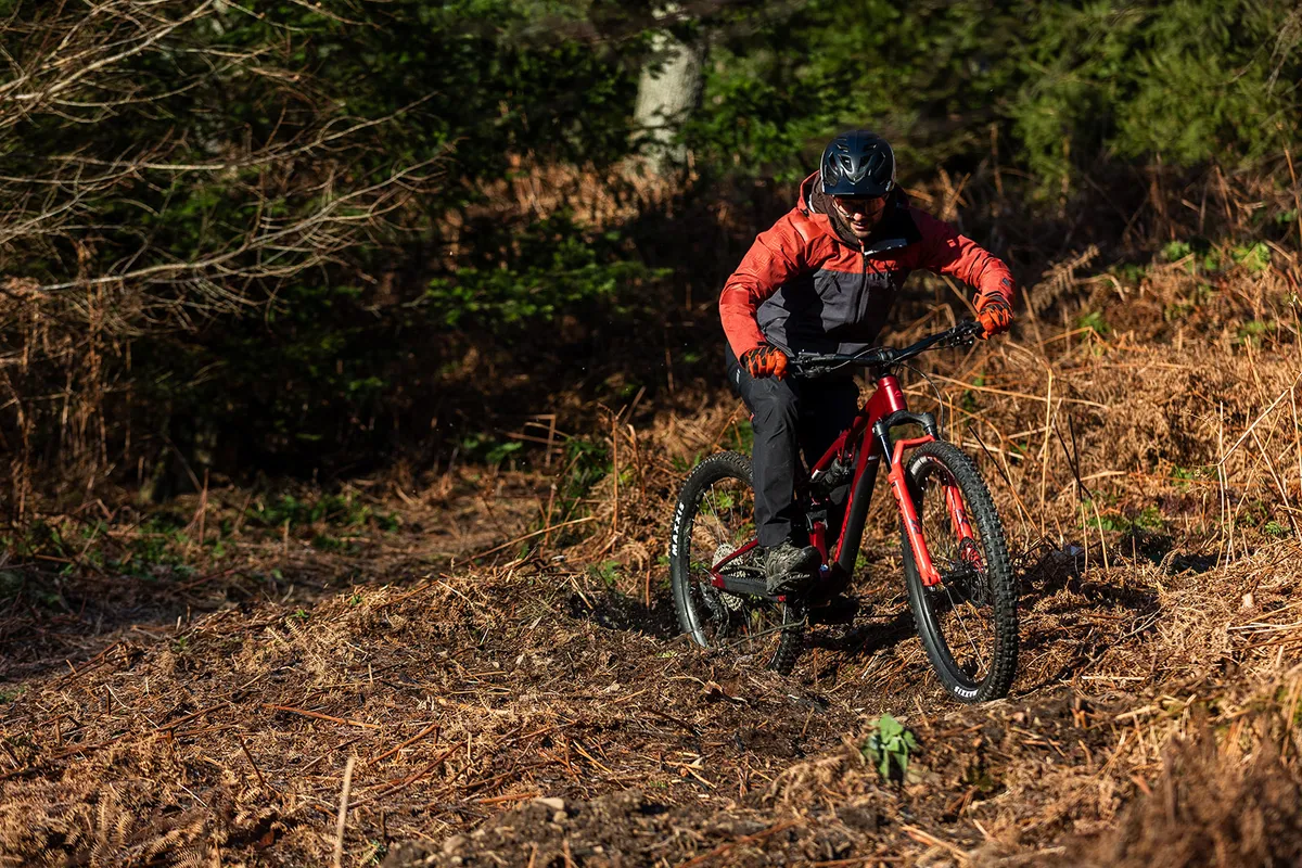 Male rider in orange and black top riding the Merida One-Forty 500 full suspension mountain bike in woodland