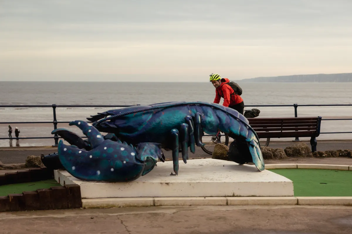 Markus Stitz riding past model lobster on seafront promenade