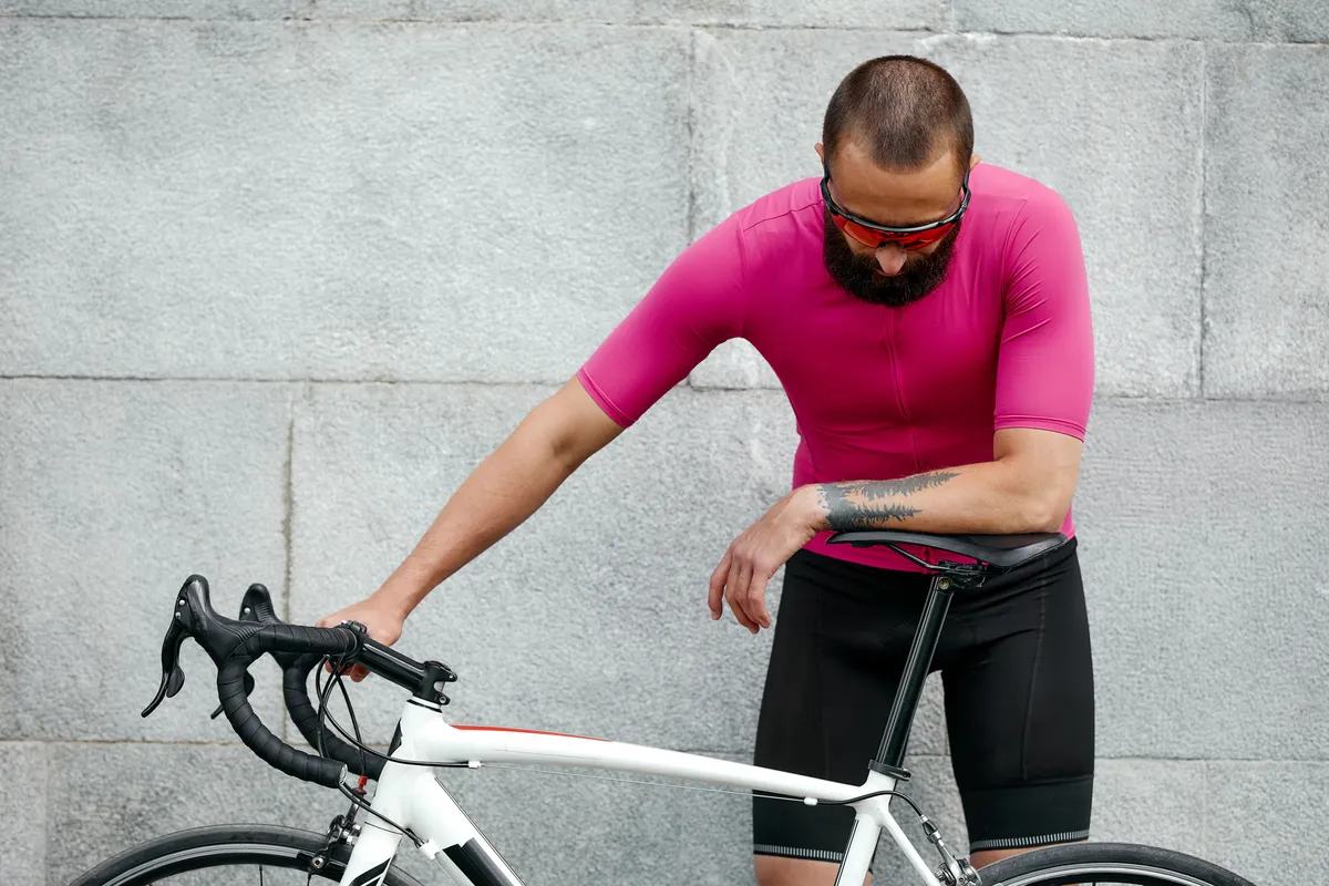 Cyclist in pink sportwear resting after an workout while standing against cement wall 