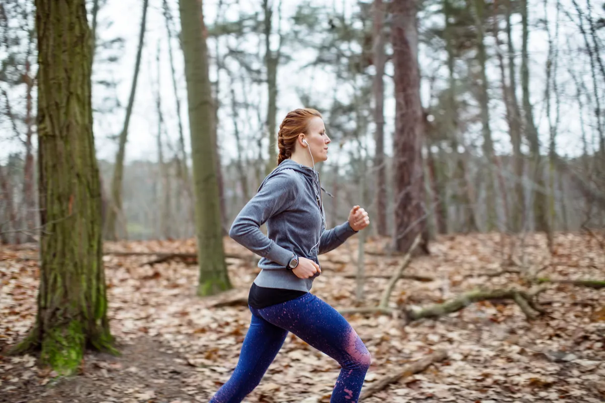 Side view of determined woman jogging in forest.