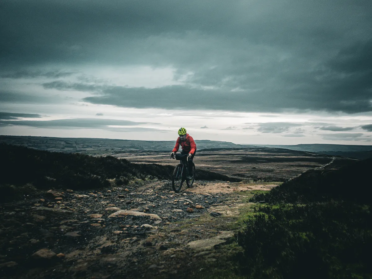Male cyclist riding up rocky moorland track