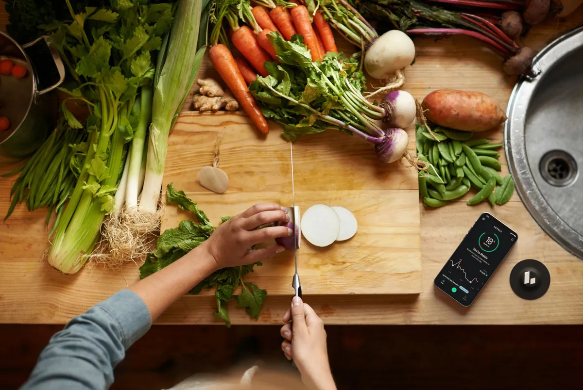 Person chopping vegetables beside Levels continuous glucose monitoring app on phone