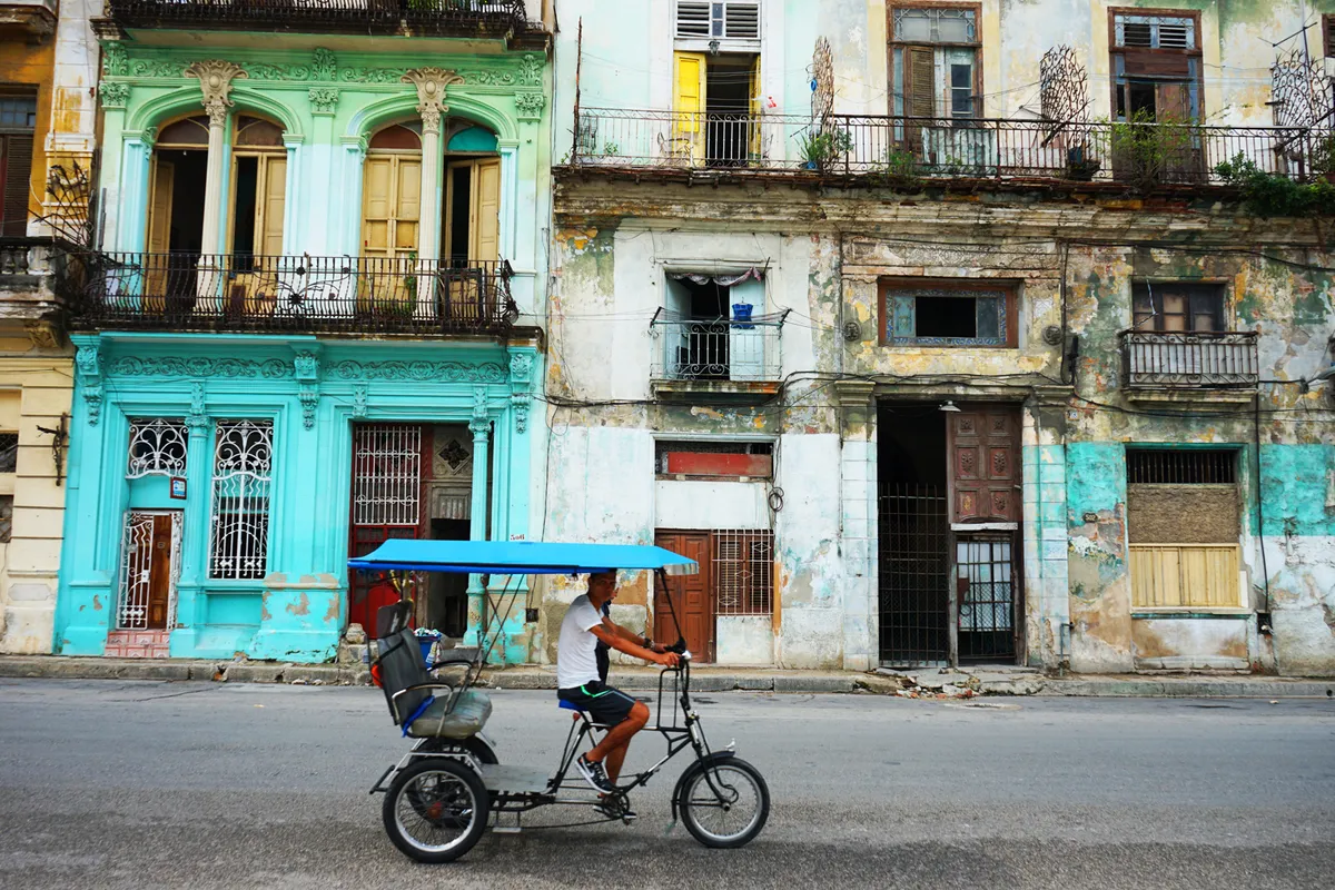 Man pedalling three-wheeled bike along street in Cuban city.