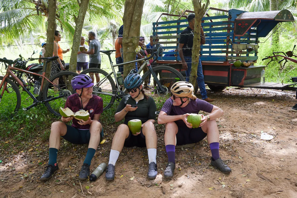 Three people sitting on ground eating coconuts in Sri Lanka.
