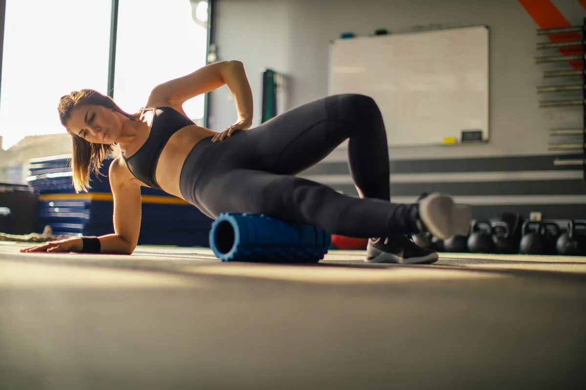 Young muscular woman using foam roller for stretching muscles after hard weightlifting training.