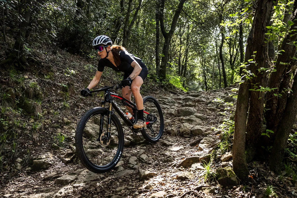 Female rider in black riding the  Pinarello Dogma XC full suspension mountain bike down hil