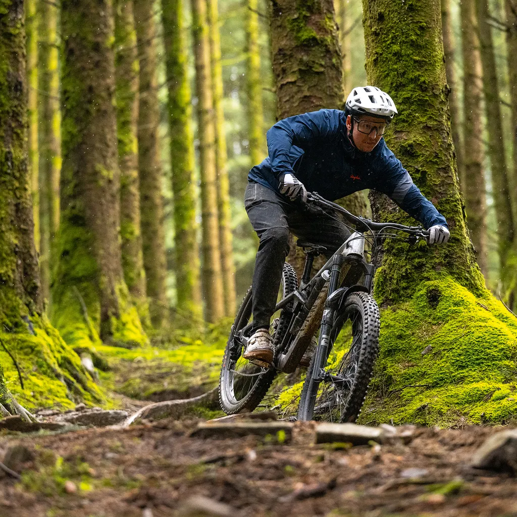 Male mountain biker Luke Marshall riding a Canyon Strive enduro mountain bike in a green and lush forest