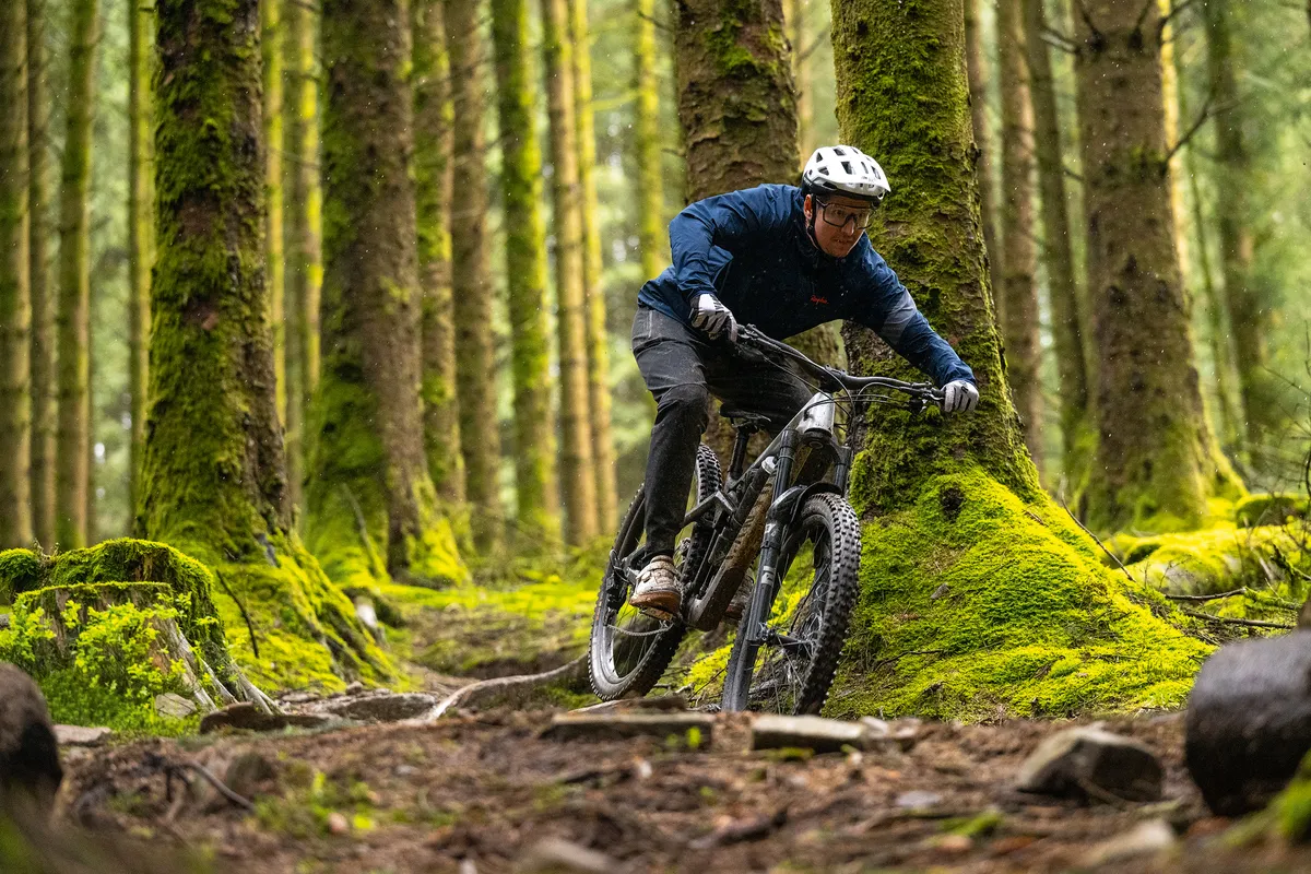 Male mountain biker Luke Marshall riding a Canyon Strive enduro mountain bike in a green and lush forest