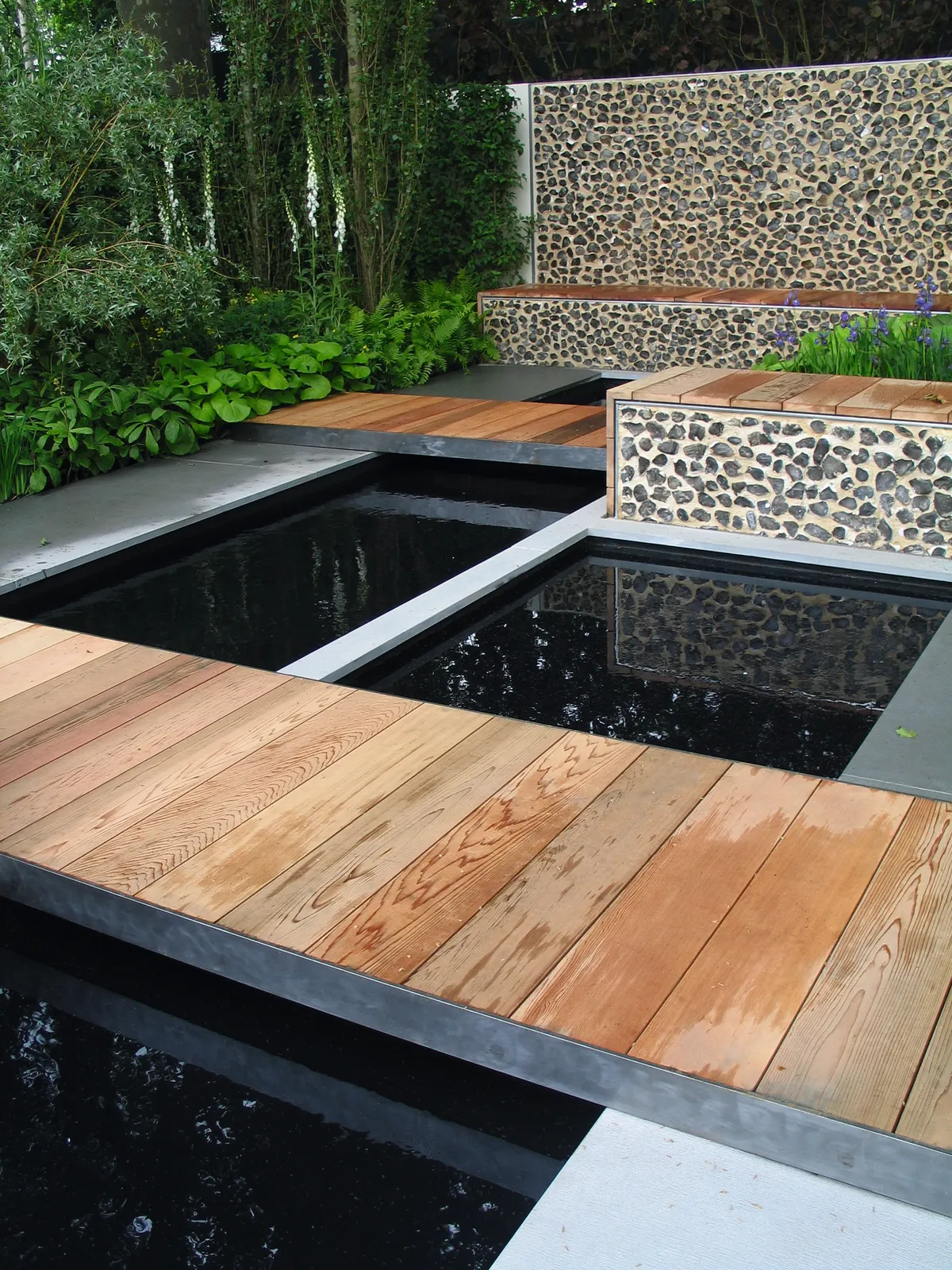 Deck pathways bridge two spaces in a contemporary garden over a mirrored pool