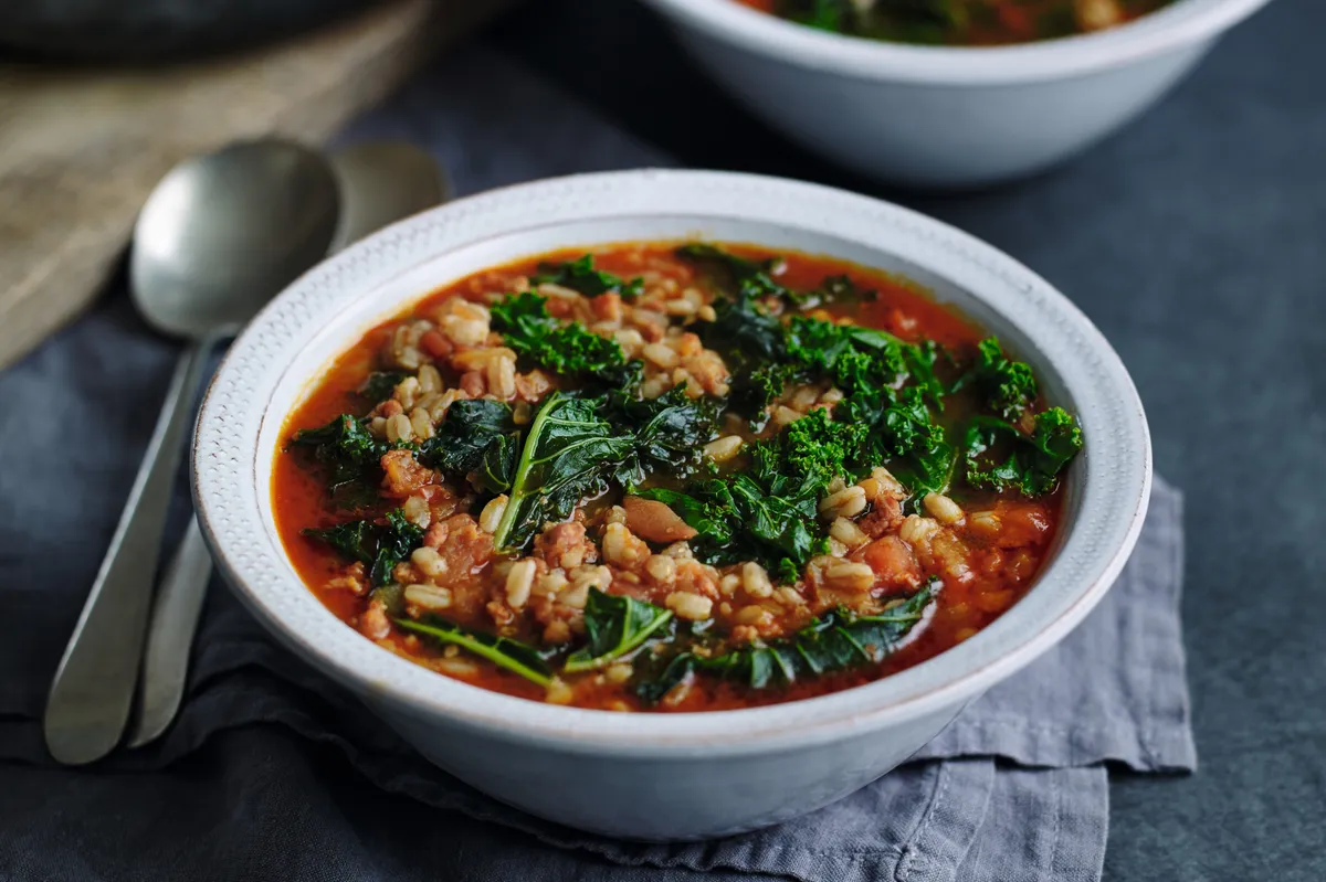 A white bowl filled with Kale, spelt and chorizo big soup placed on on a laid table