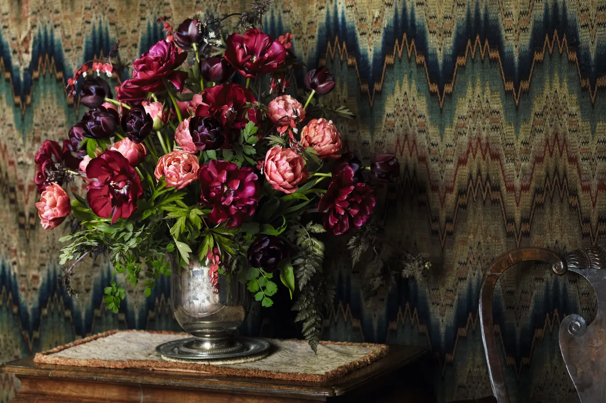 A photograph depicting a sumptuous floral arrangement of tulips in contrasting colours of deep reds, dark purple and light pink