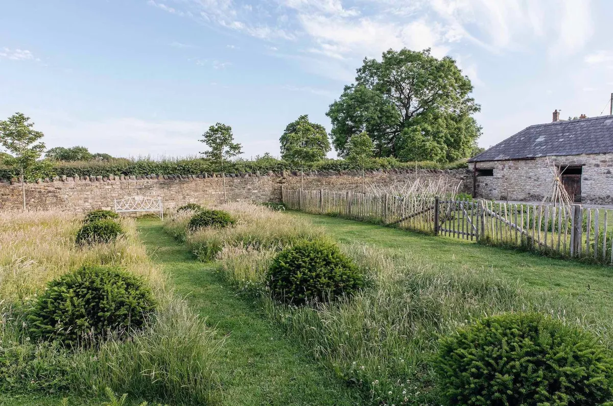 The Willow Garden, a simple but effective grid of rumpled yew domes set in long grass with an inviting bench that catches the evening sun. Beyond the paling fence is the Vegetable Garden.