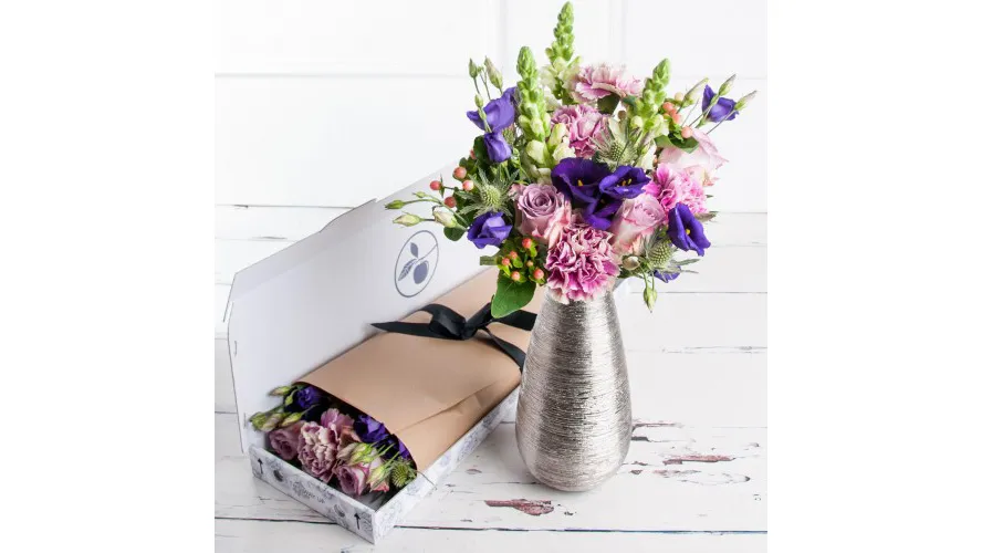 A bouquet of flowers in a vase and a flower subscription box on a wooden table.