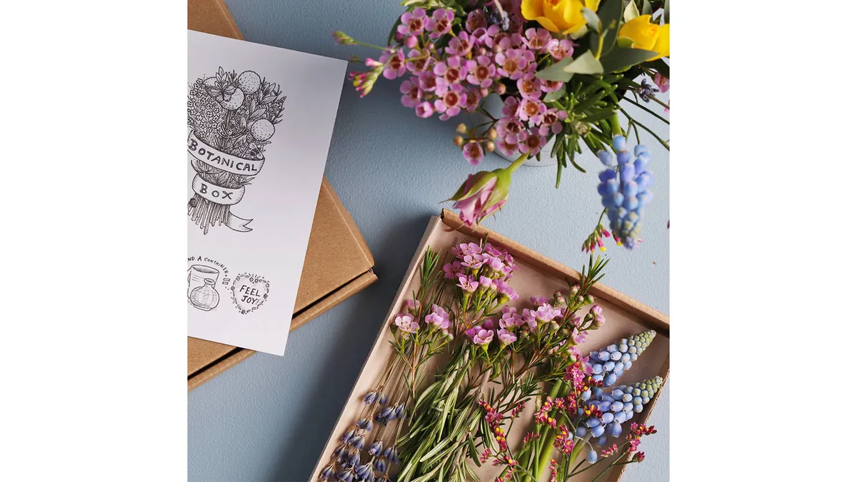 Flowers in a cardboard box and vase next to a white card.