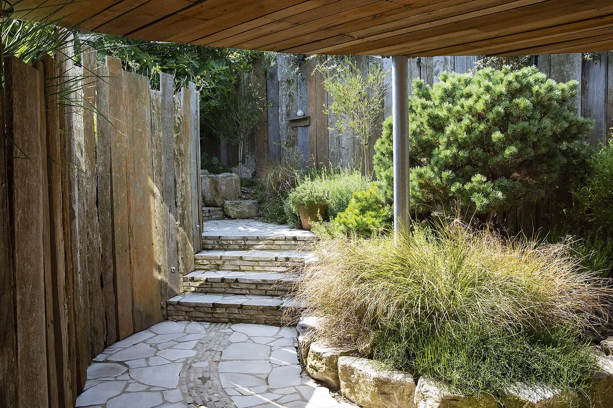 A Purbeck stone path with steps winds under the terrace, framed by stone walls and pheasant grass Anemanthele lessoniana