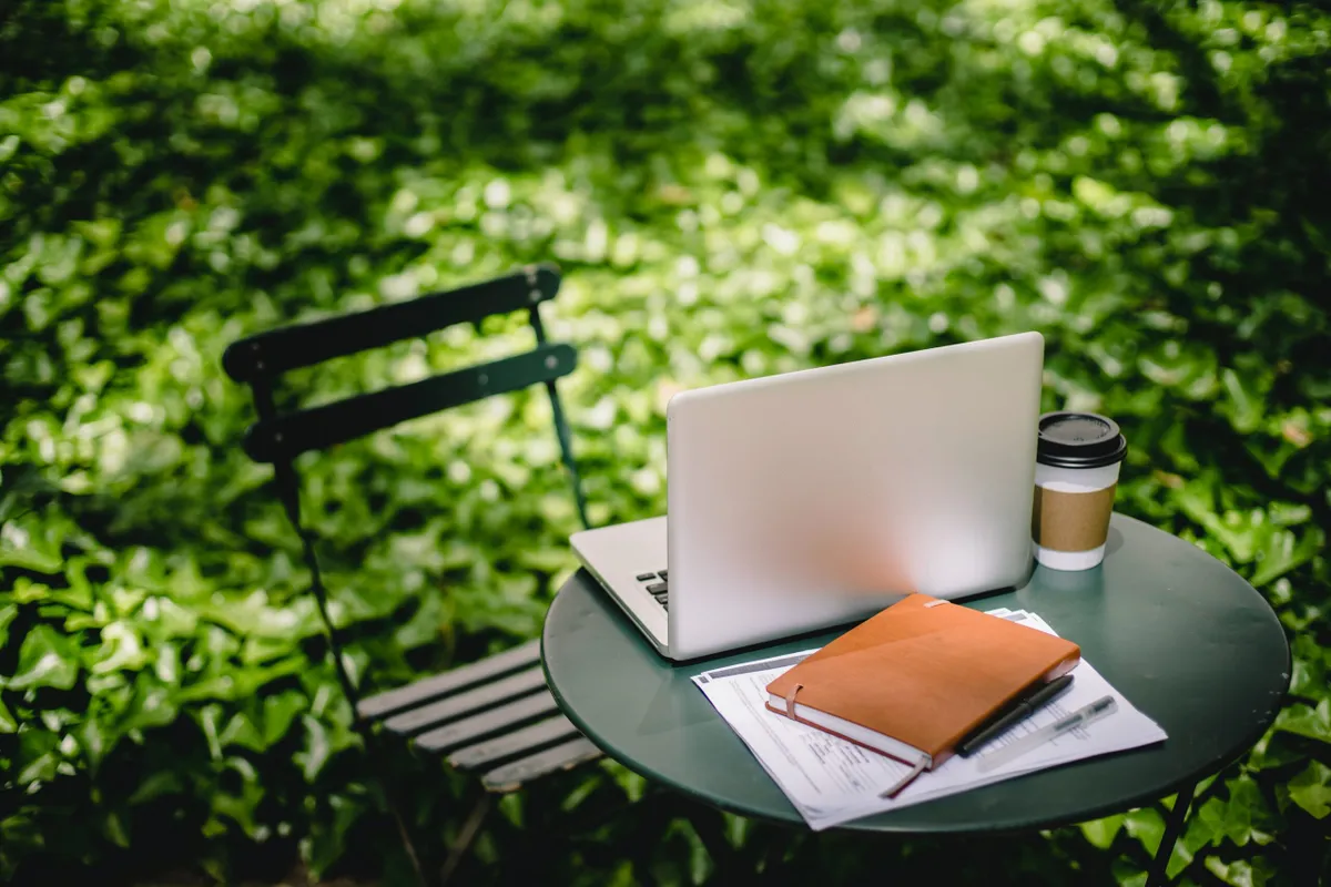 Laptop, coffee and notebook on a garden table