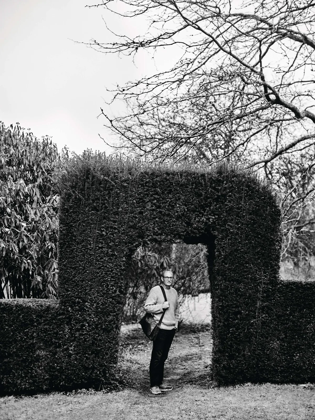 Black and white image of man stood under a hedge arch