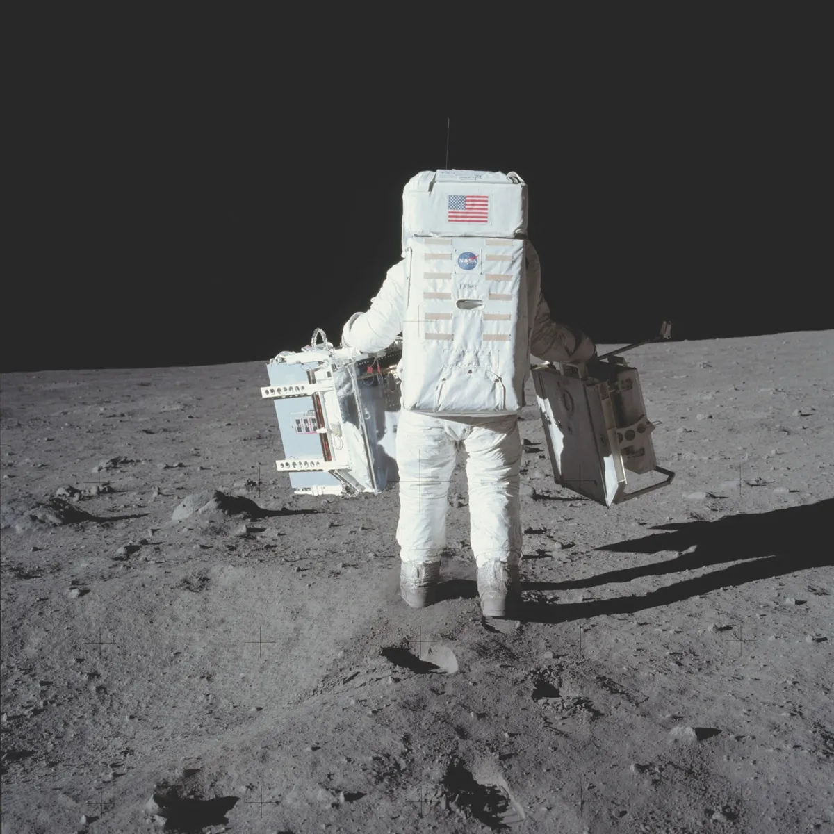 Reduced lunar gravity makes it easy for Aldrin to carry a pair of experiment packages for deployment © NASA/JPL