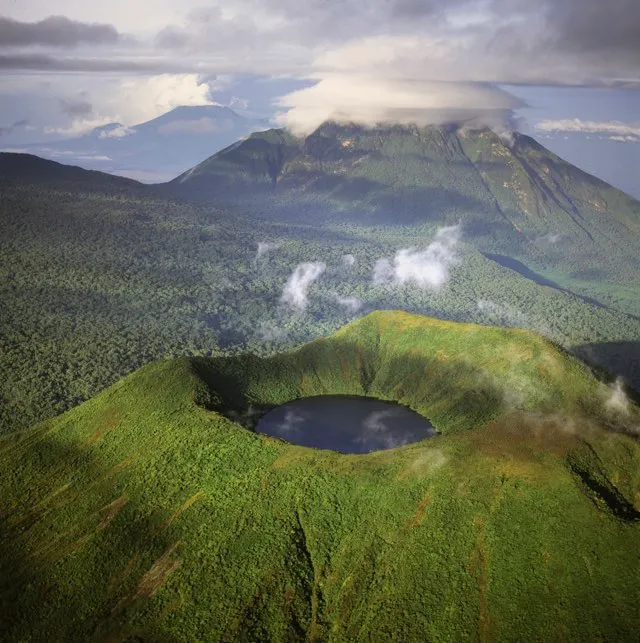 Aerial view of Mount Visoke (Mount Bisoke), an extinct volcano straddling the border of Rwanda and Democratic Republic of the Congo (DRC) showing crater lake, with Mount Mikeno in background, Virunga Volcanoes, Great Rift Valley, Africa - stock photo