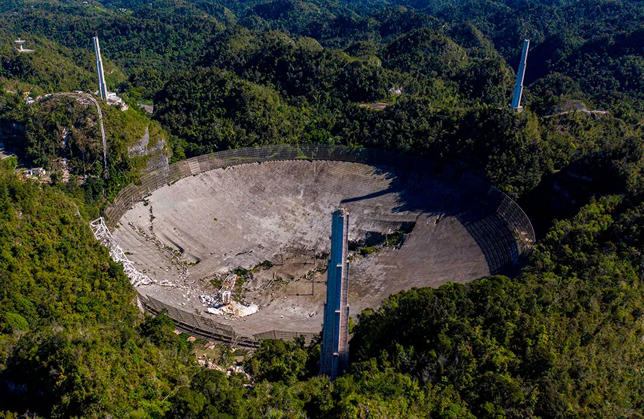 TOPSHOT - This aerial view shows the damage at the Arecibo Observatory after one of the main cables holding the receiver broke in Arecibo, Puerto Rico, on December 1, 2020. - The radio telescope in Puerto Rico, which once starred in a James Bond film, collapsed Tuesday when its 900-ton receiver platform fell 450 feet (140 meters) and smashed onto the radio dish below