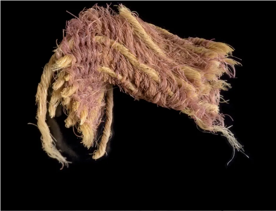 A wool textile fragment decorated with pink-purple weft threads