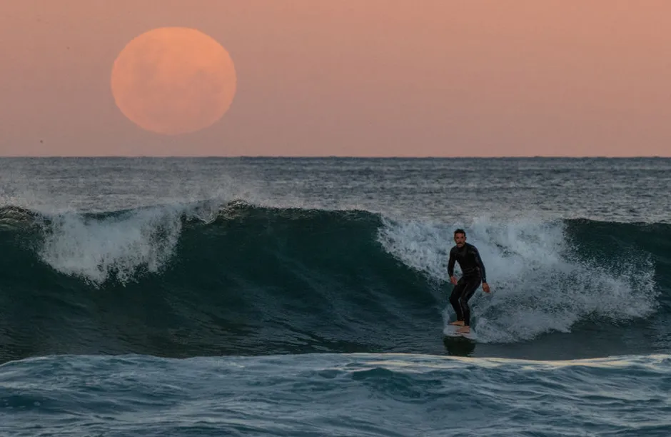 A surfer rides a wave as a super blood moon rises above the horizon at Manly Beach on May 26, 2021 in Sydney, Australia. It is the first total lunar eclipse in more than two years, which coincides with a supermoon. A super moon is a name given to a full (or new) moon that occurs when the moon is in perigee - or closest to the earth - and it is the moon's proximity to earth that results in its brighter and bigger appearance. (Photo by Cameron Spencer/Getty Images)