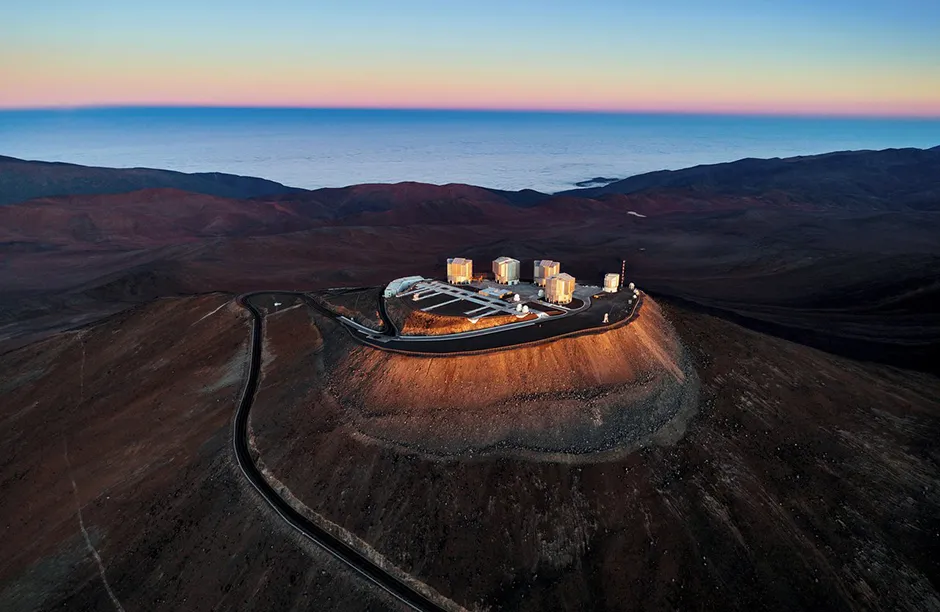 In this image, the first rays of the morning Sun shine down upon Cerro Paranal in northern Chile, the home of ESO's Very Large Telescope (VLT) — signalling that another successful night of observations has concluded at the world’s most productive ground-based astronomical facility. Rising 2635 metres above sea level, the VLT’s site is amongst the best in the world for gazing deep into the Universe. Giving a sense of the site’s altitude is the apparent “sea” in the background. This is, however, a trick of the eye; the Atacama Desert, where ESO’s VLT is located, is a very dry place. Rather than liquid water, the distant, blue-hued sea is instead composed of clouds that form at lower elevations. Link: Panoramic image of the VLT