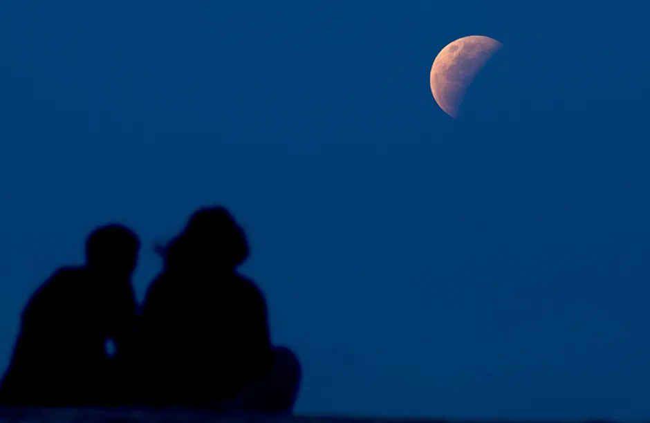 Photo by Firdia Lisnawati/AP/Shutterstock (11973378a) Couple watch the lunar eclipse at Sanur beach in Bali, Indonesia on . The total lunar eclipse, also known as a super blood moon, is the first in two years with the reddish-orange color the result of all the sunrises and sunsets in Earth's atmosphere projected onto the surface of the eclipsed moon Lunar Eclipse , Bali, Indonesia - 26 May 2021