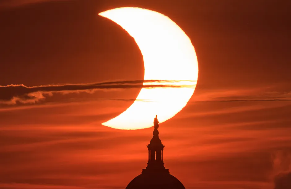A partial solar eclipse is seen as the sun rises behind the United States Capitol Building, Thursday, June 10, 2021, as seen from Arlington, Virginia. The annular or “ring of fire” solar eclipse is only visible to some people in Greenland, Northern Russia, and Canada. Photo Credit: (NASA/Bill Ingalls)