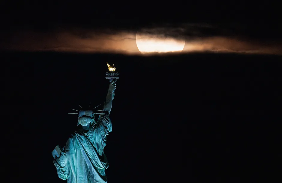 The full moon, known as the strawberry moon, rises behind the Statue of Liberty in New York City on June 24, 2021. - The first full moon of summer 2021, also known as the Strawberry Moon, rises June 24, marking the last supermoon of the year. June's full moon is often referred to as the Strawberry Moon because it falls during the strawberry harvesting season in the northeastern US. Similarly, June's full moon has also been called the Rose Moon because it occurs around the time roses bloom. (Photo by Angela Weiss / AFP) (Photo by ANGELA WEISS/AFP via Getty Images)