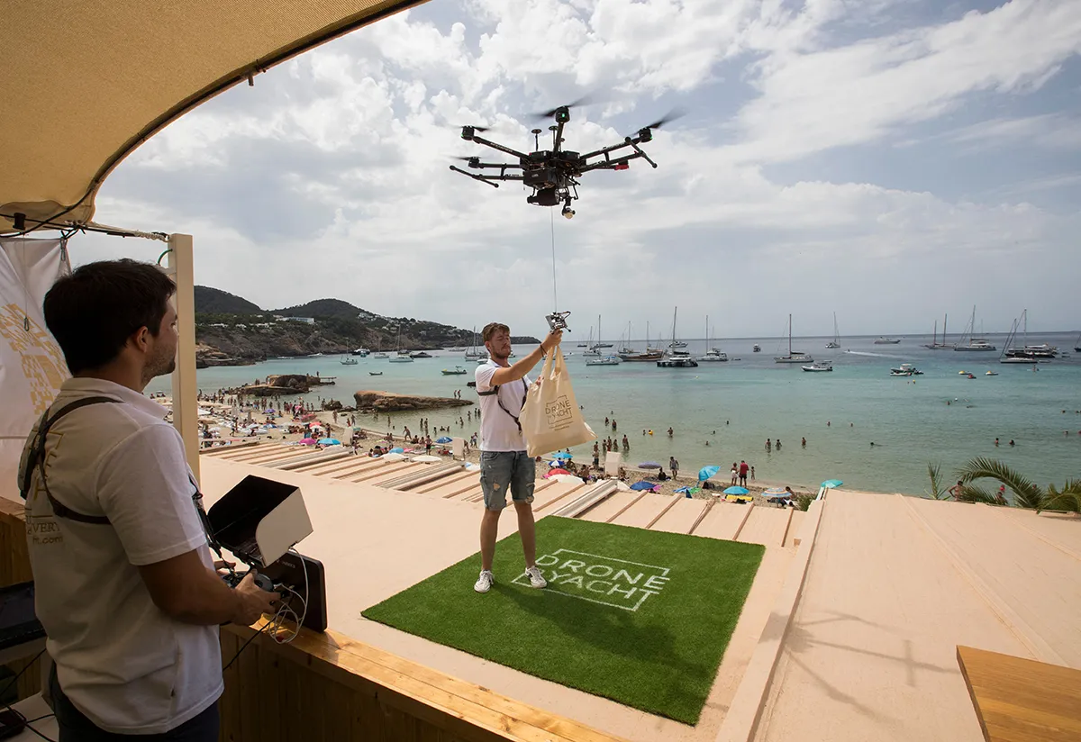 A drone pilot ties up a bag of food to a drone at Cala Tadira near Sant Josep de Sa Talaia in Ibiza Island on August 24, 2021. Drone to Yacht is an exclusive delivery service for yachts launched in Ibiza by the restaurant Can Yucas and the Galician company Aerocamaras to deliver food and drinks to yachts. (Photo by JAIME REINA / AFP) (Photo by JAIME REINA/AFP via Getty Images)