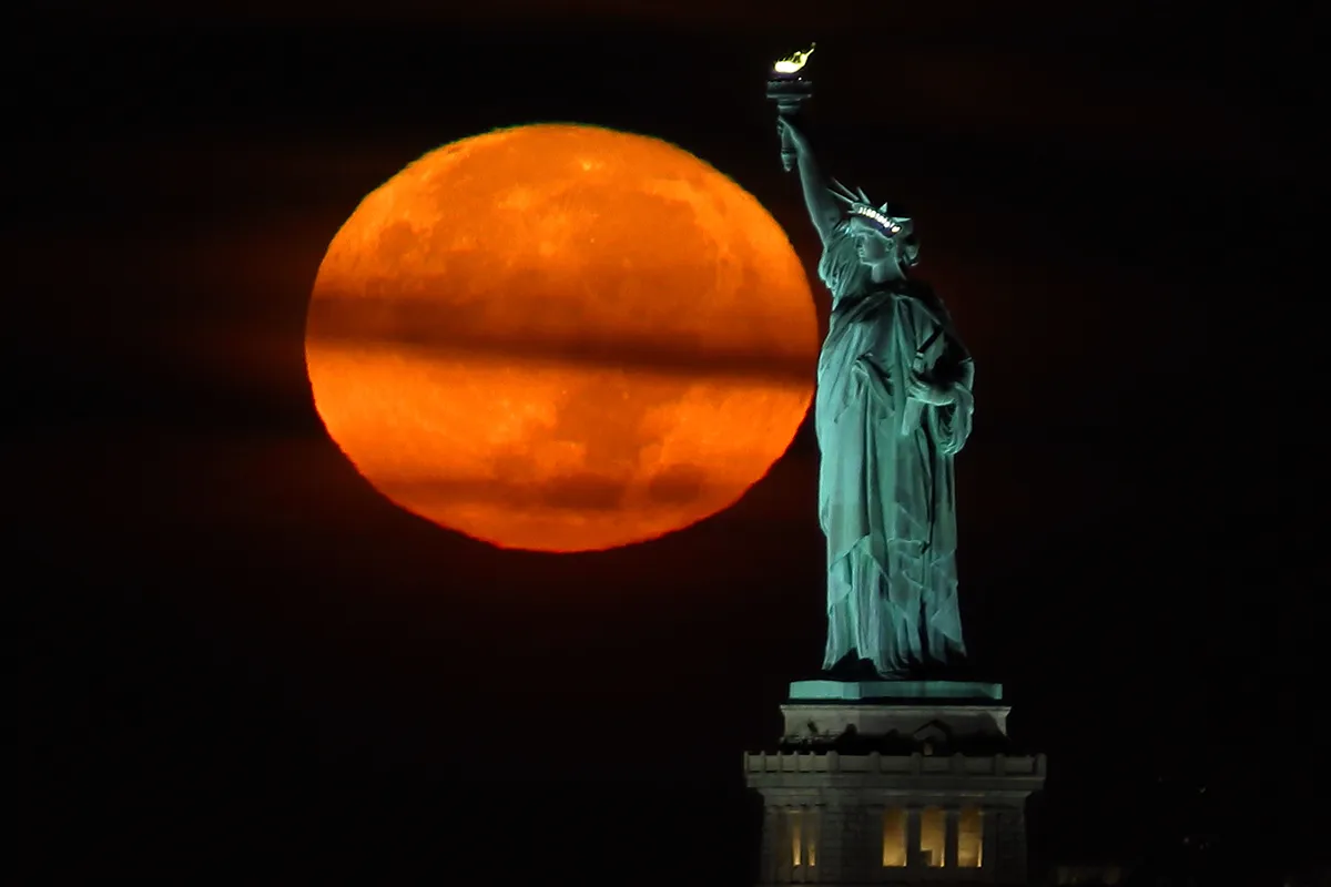 NEW YORK, NY - SEPTEMBER 20: The Harvest Moon sets behind the Statue of Liberty before sunrise on September 20, 2021 in New York City. (Photo by Gary Hershorn/Getty Images)